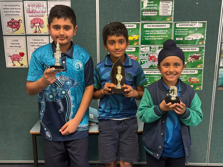 Three students holding chess trophies.