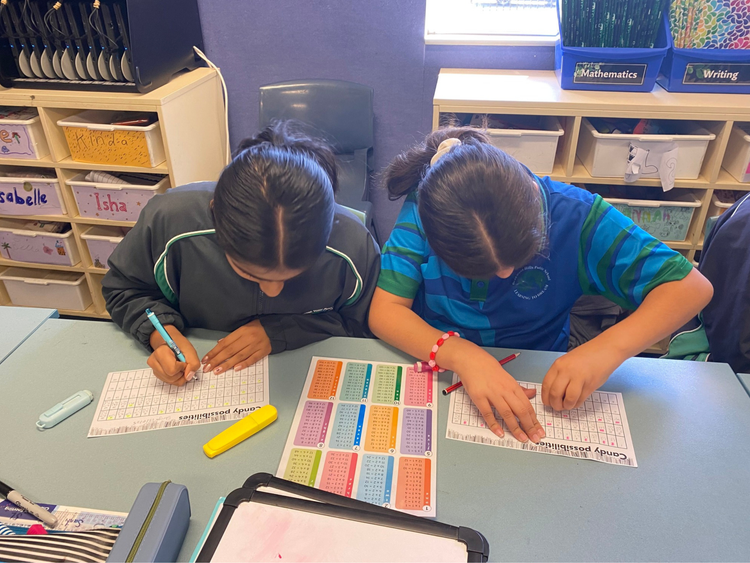 Two students completing maths activities at their desk.